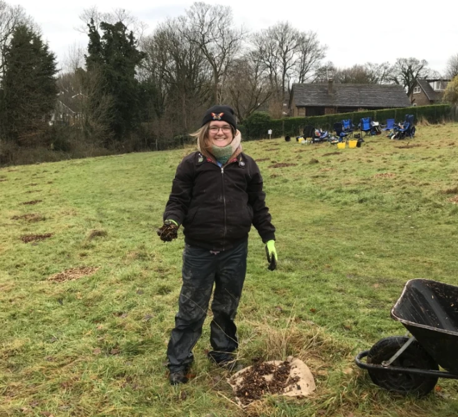 Yeva holding soil by a sapling planting site, smiling and dressed for cold weather.