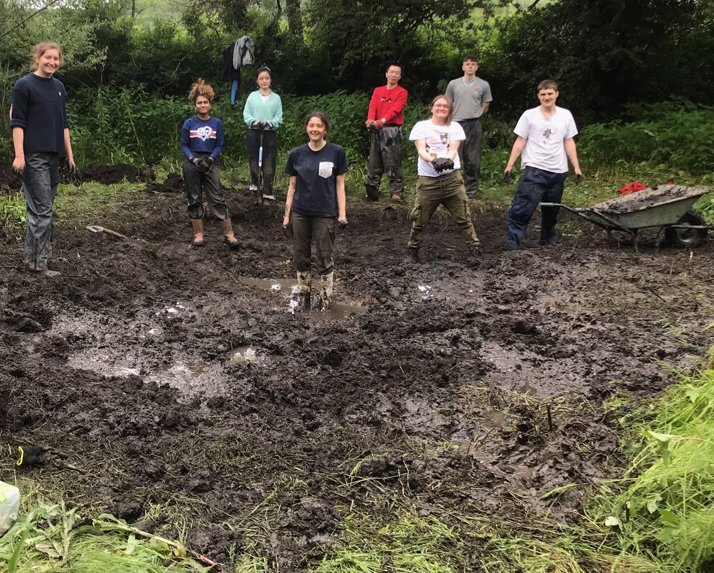 a group of young people posing in a muddy freshly-dug pond