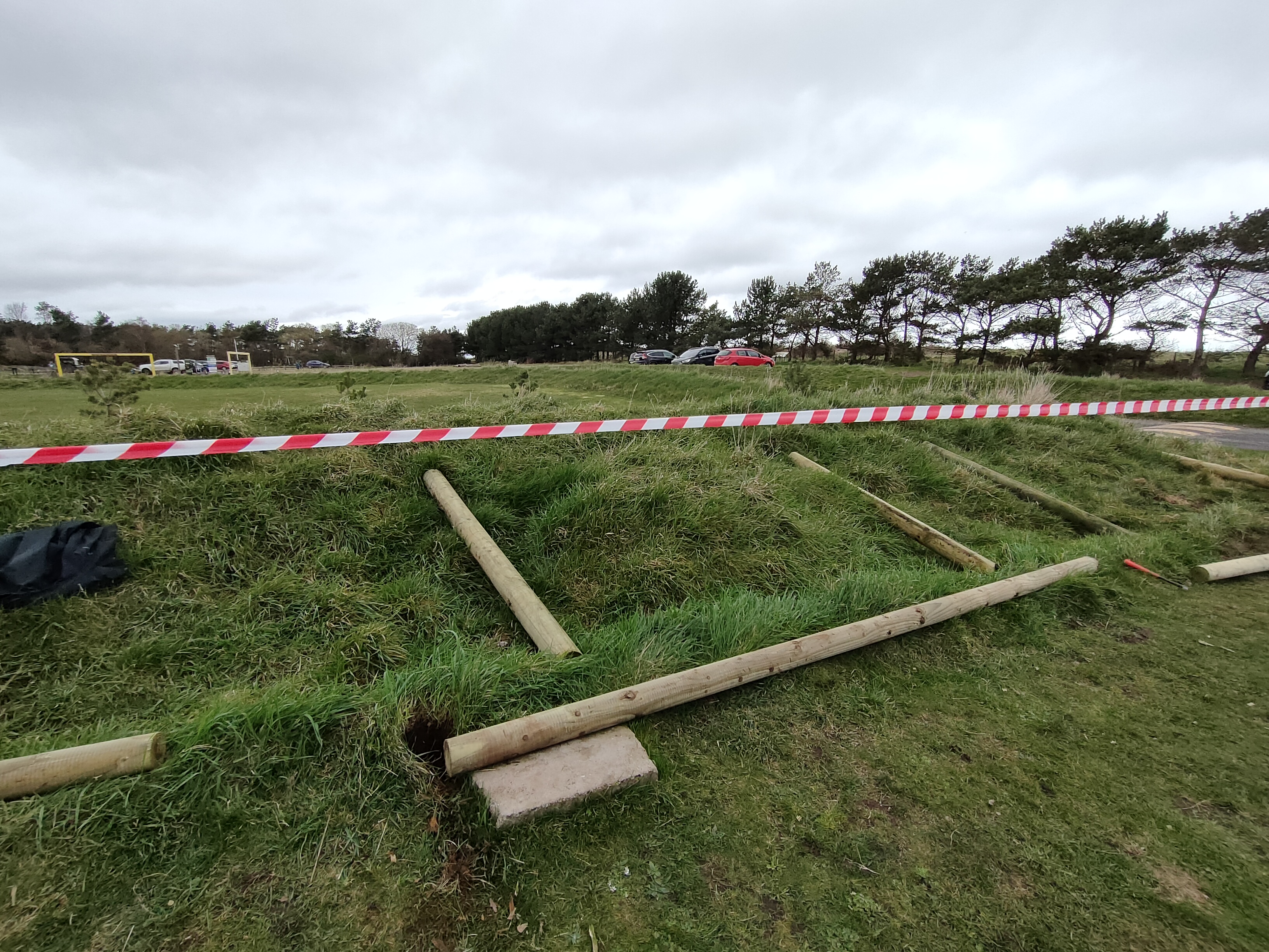 Cylindrical fence posts on the ground next to deep holes.