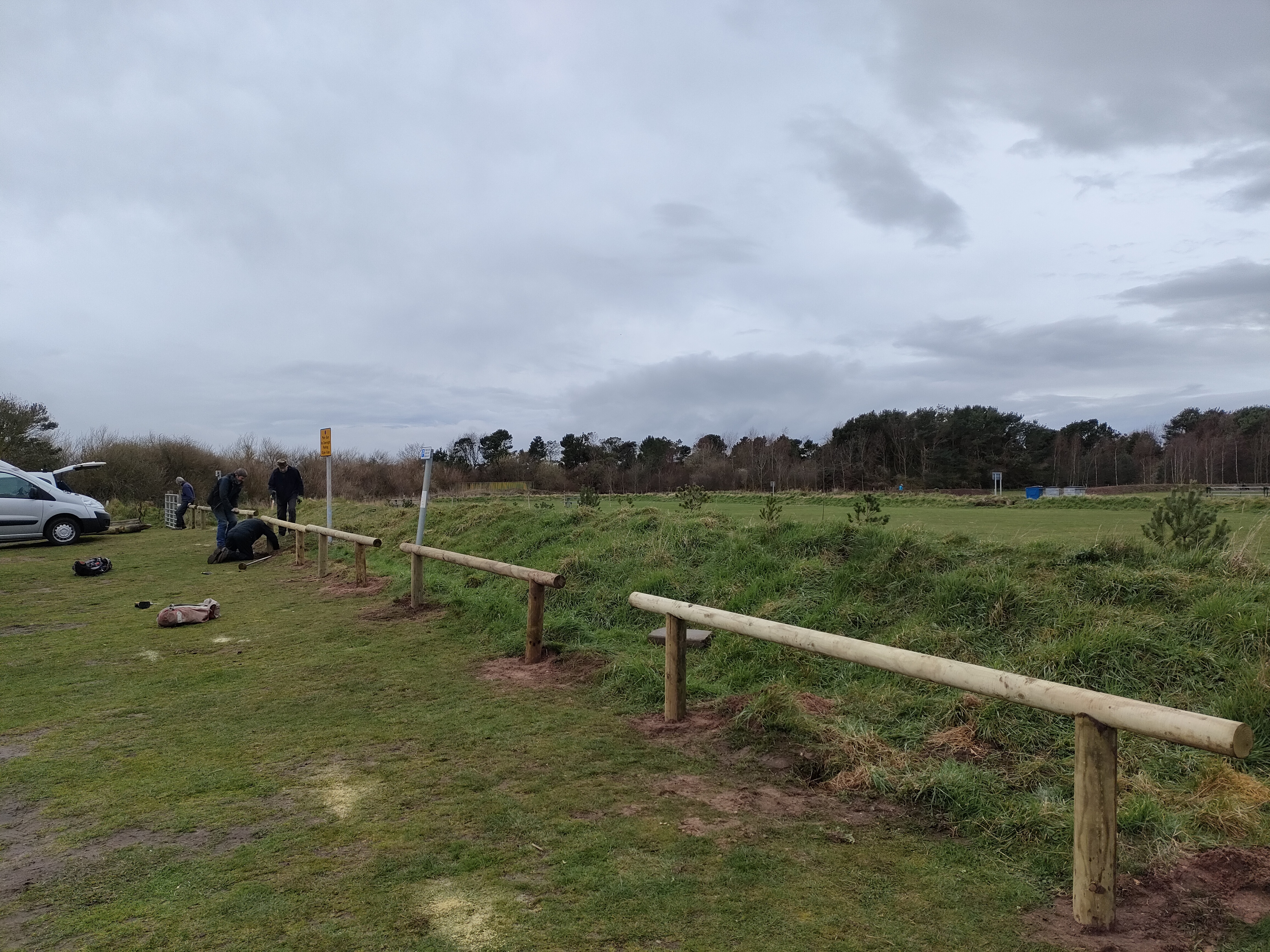 A low wooden fence at the perimeter of a car park.